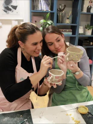 Dos alumnas pintan tazas en un taller de cerámica